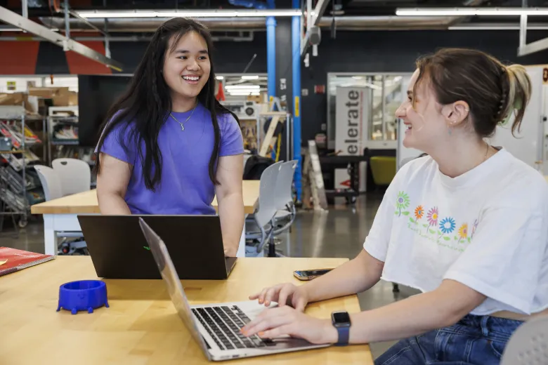 Two students on laptops laughing 