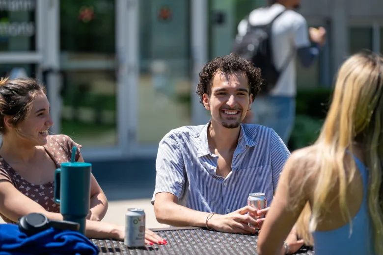 A male and two female students laugh with each other on the Wentworth quad.
