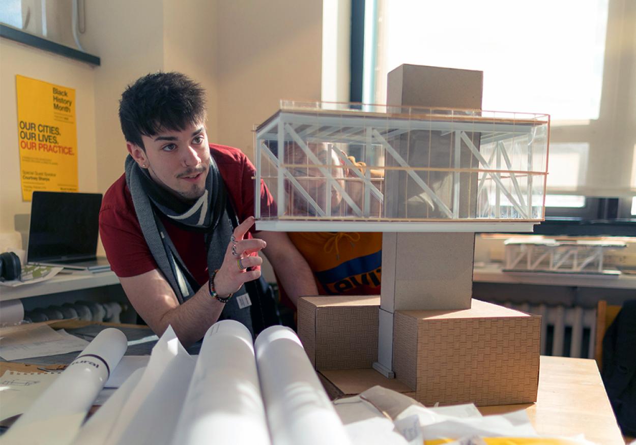 A male architecture student examines a cardboard model.