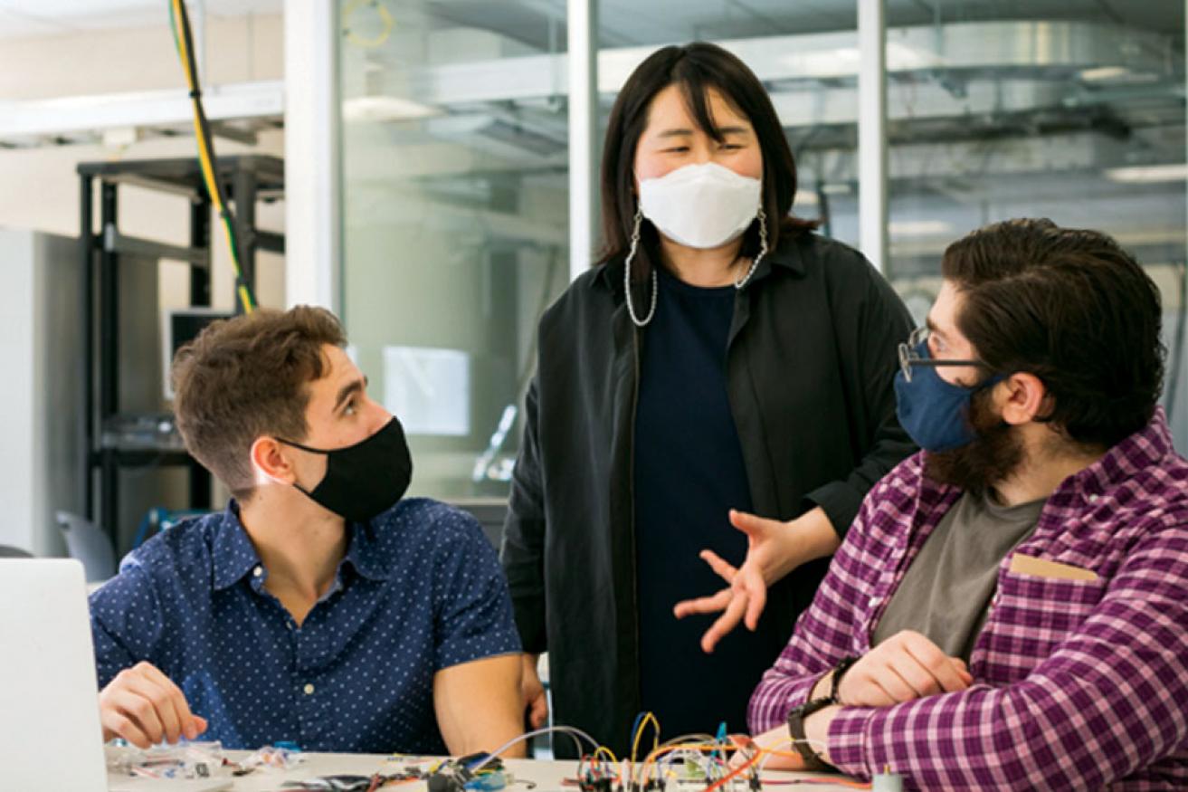 A female faculty member is talking to two students.