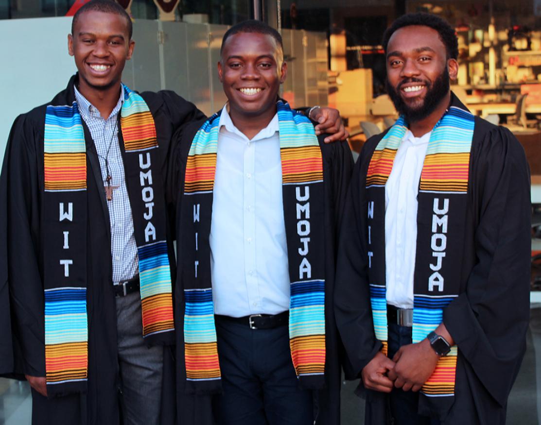 Three students in graduation robes with UMOJA scarves around their necks.