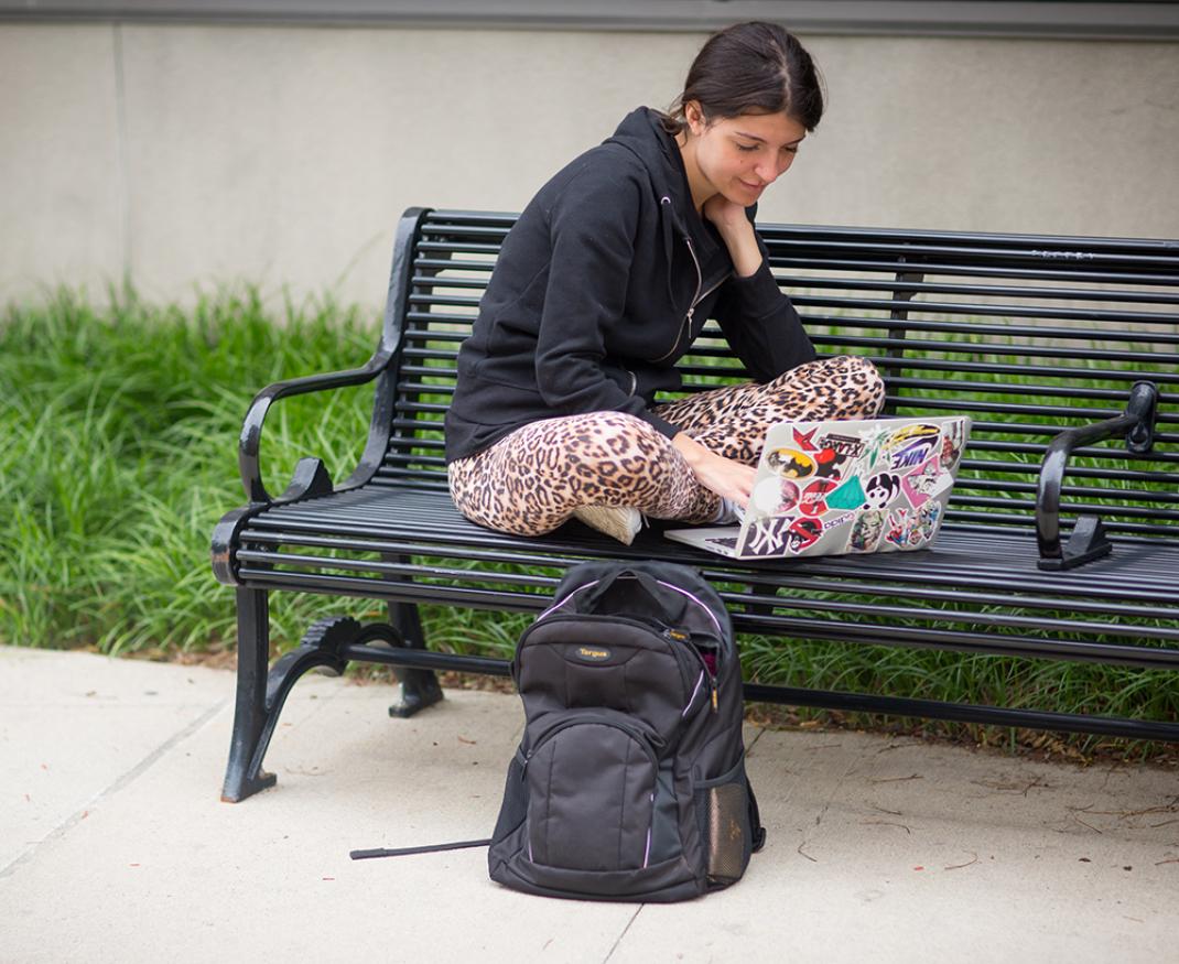 Woman sitting on bench working on laptop.