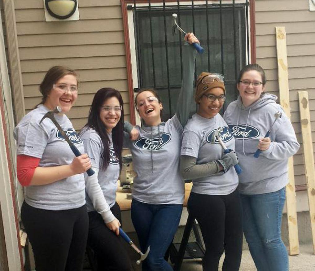 A group of female students holding hammers at building site.