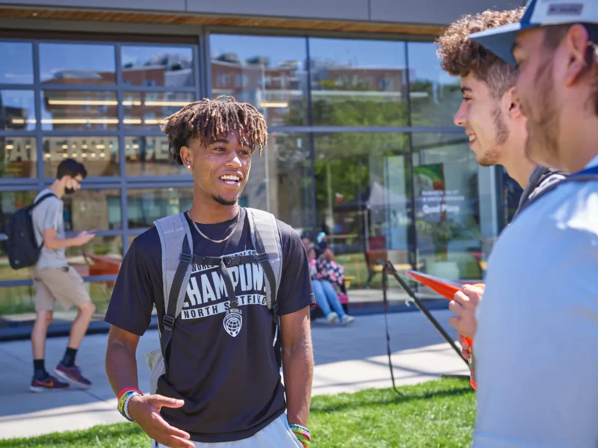 Three male students talk on the quad in front of the CEIS building