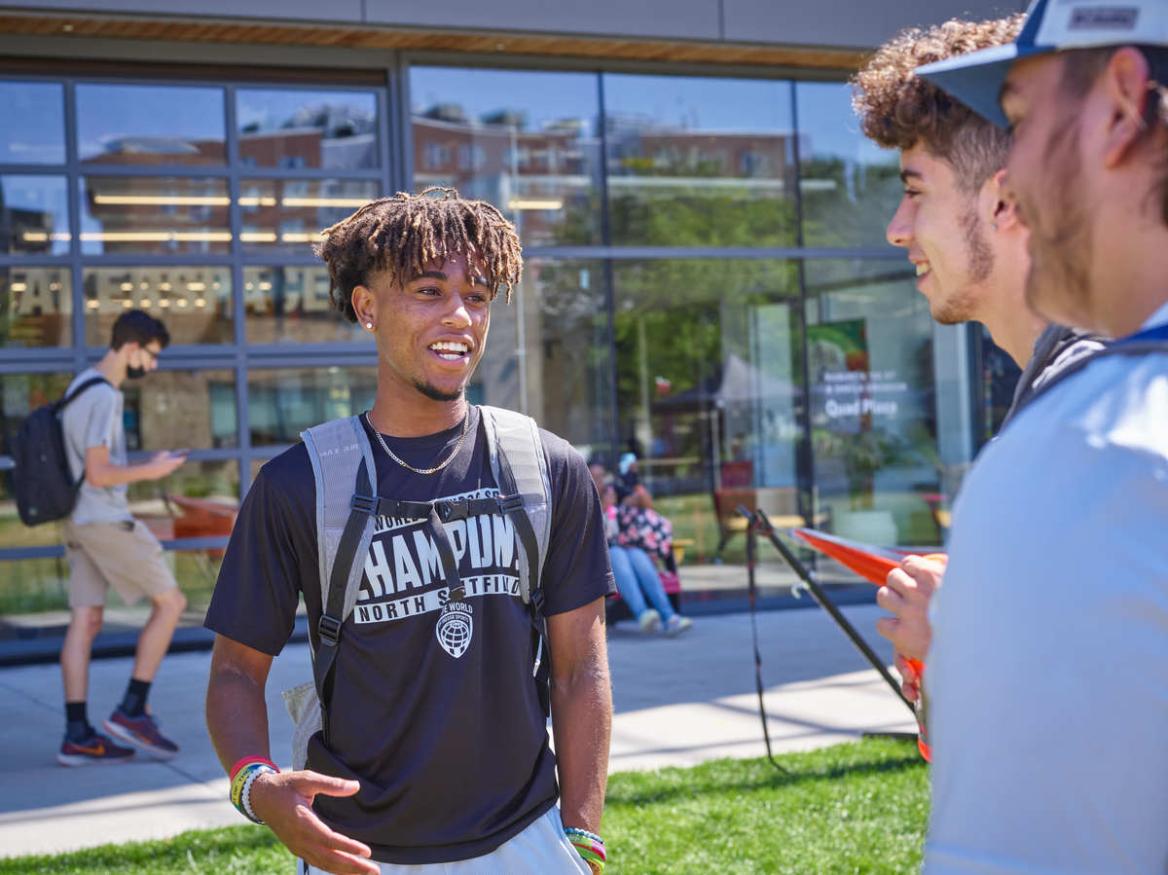 Three male students talk on the quad in front of the CEIS building