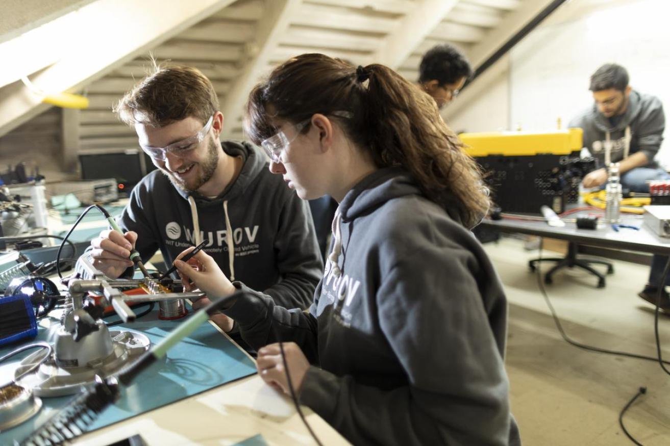 Two students work on a robotics project together by soldering