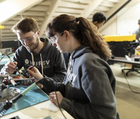 Two students work on a robotics project together by soldering