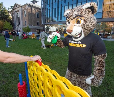 Ruggles the leopard campus mascot plays connect four with participants on the quad during Wentworth Weekend