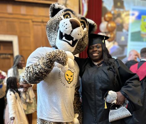 a woman in a graduation robe poses with a leopard mascot
