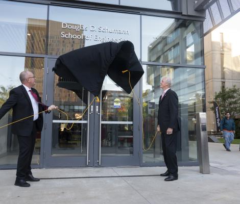 two men remove a covering on a building to reveal a new sign