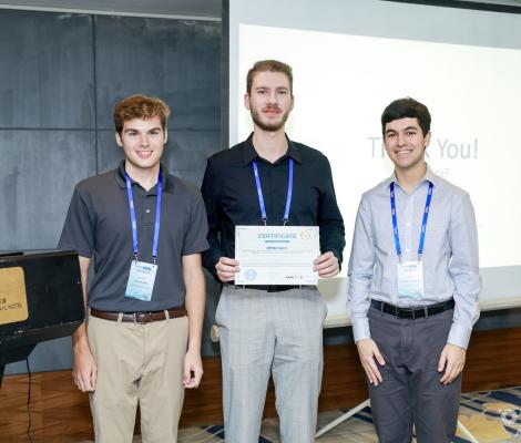 three students stand while one holds a certificate