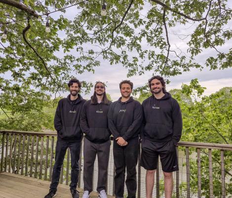 a group of four people pose in black sweatshirts in front of trees