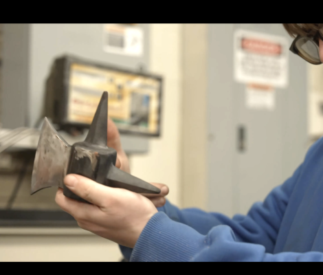 a student holds up a steel axe part