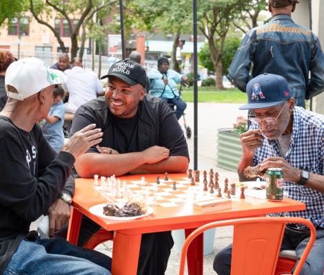 three men having a chat over a chess board outdoors