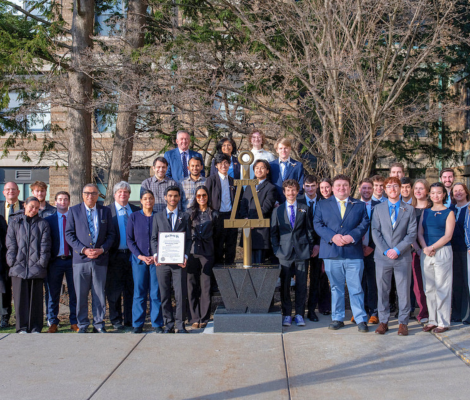 a large group of people pose in front of a statue on a college campus