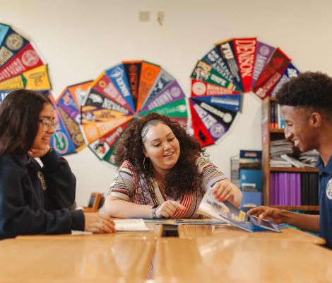three people sit at a table with college banners on the walls behind them