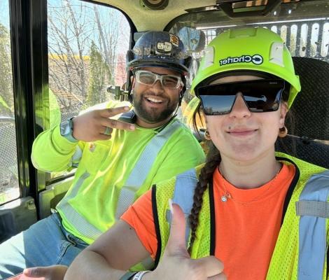 two people in hard hats and vests witting in an excavator