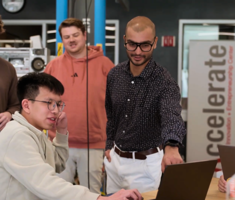 students and a professor look at a computer screen together