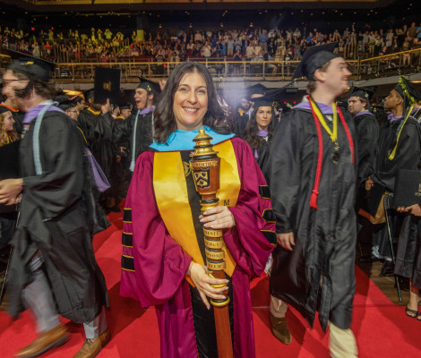 a woman in a graduation robe is surrounded by students in graduation robes in an indoor arena