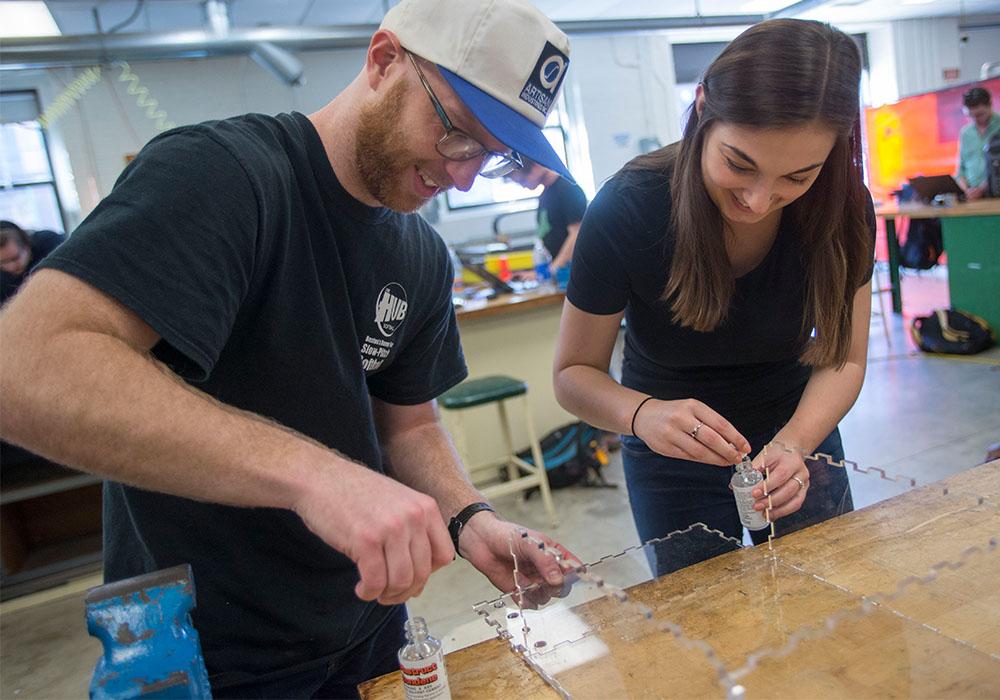 Two students working on engineering project with plexiglass