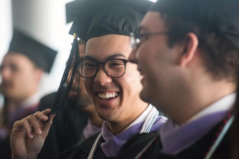 Two men in caps and gowns laugh while waiting to walk across stage.