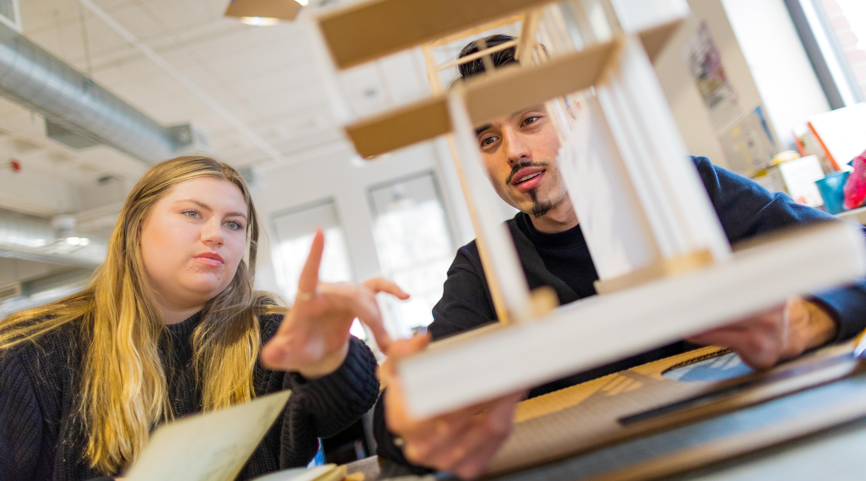 A female and male student examine an architectural model. 