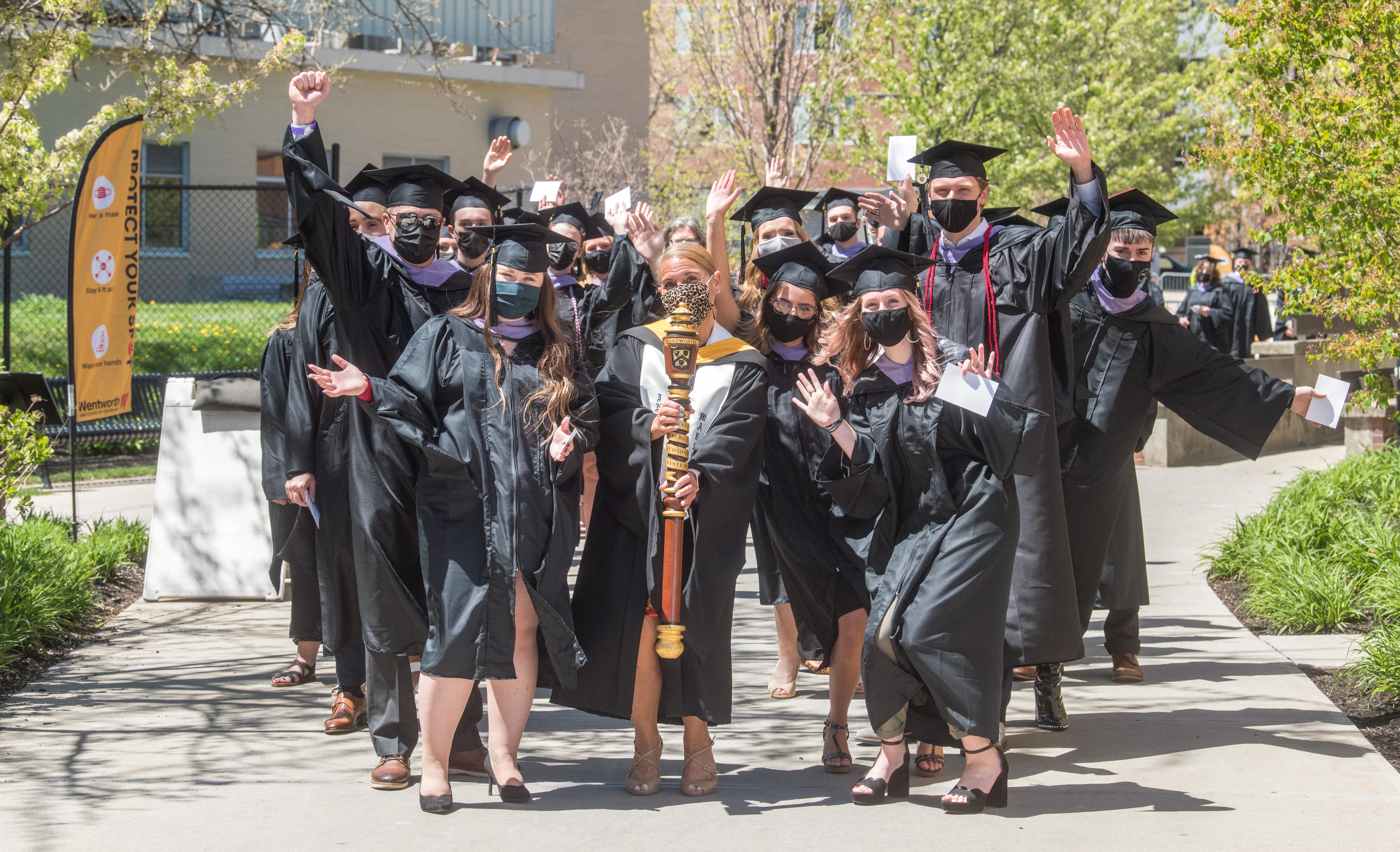 students in caps and gowns waiting to graduate - celebratory pose wearing masks due to Covid-19