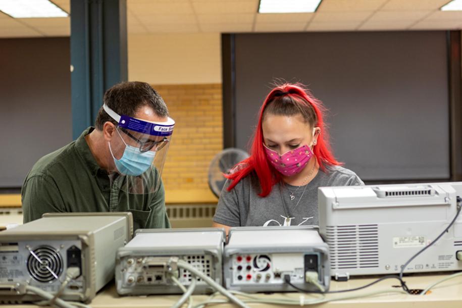 A professor and student stand side-by-side working on a project