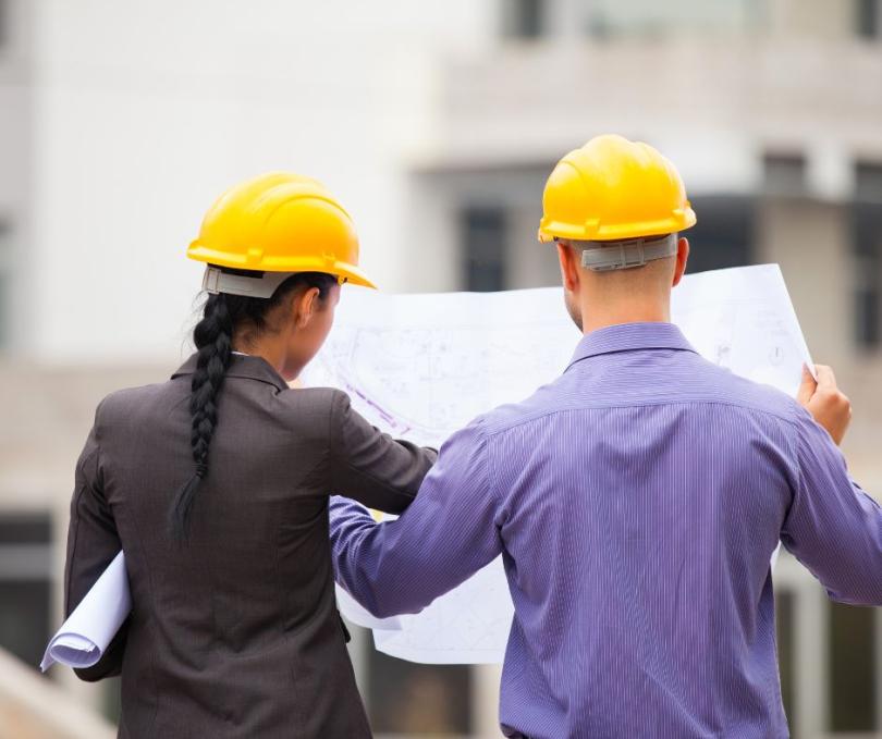 two people in hard hats look at blueprints