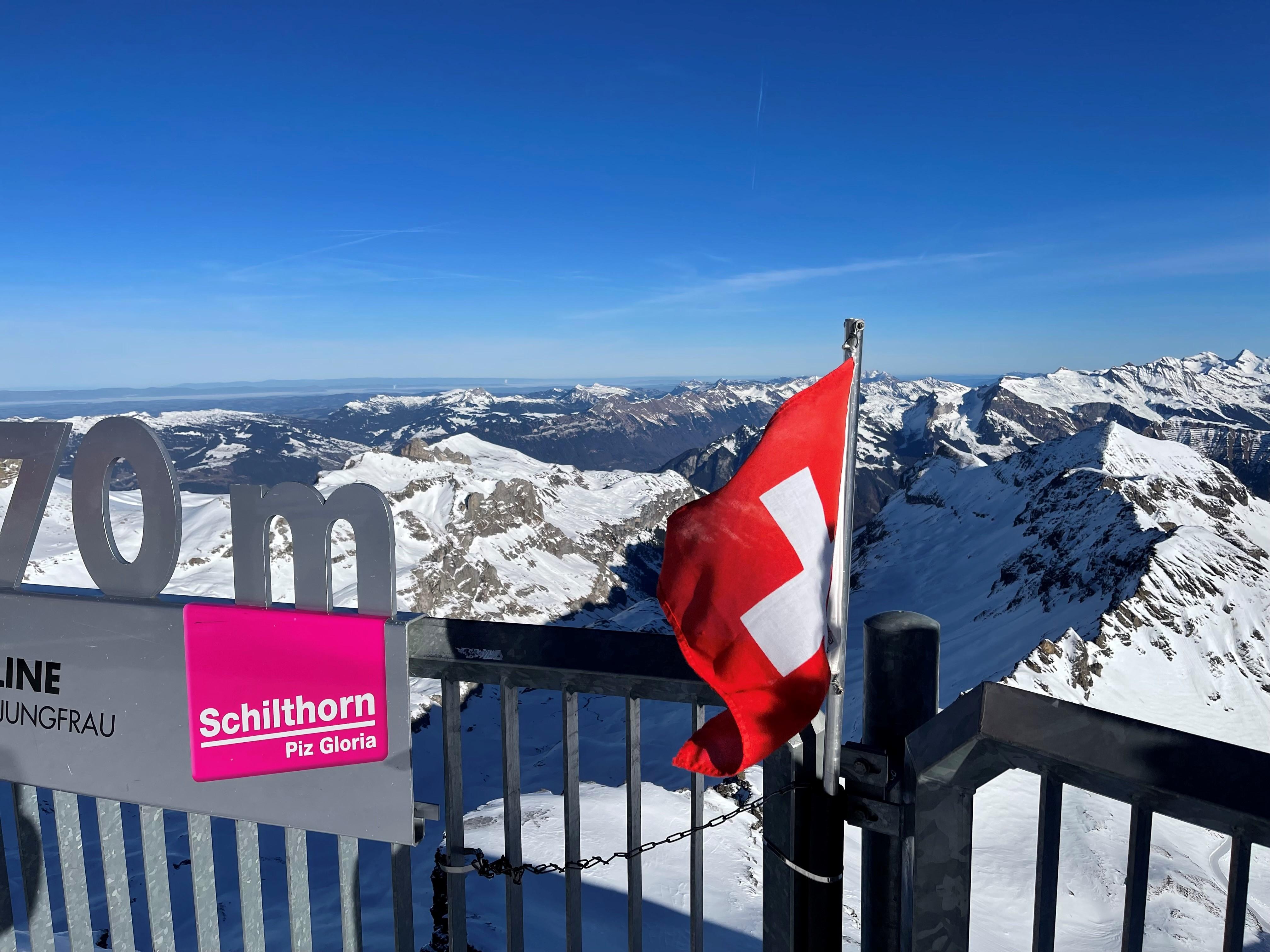 A photo of the snow covered Swiss Alps with a Swiss flag in front