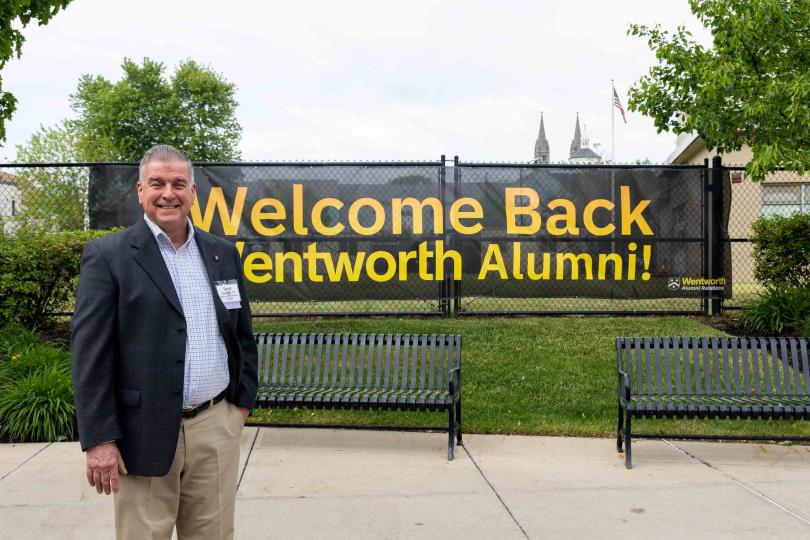 a man stands in front of a banner reading "alumni"