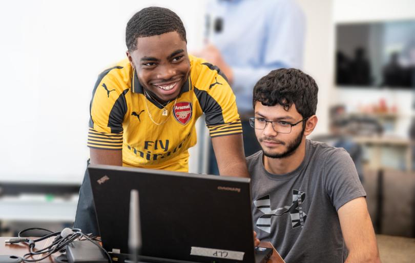 Two male students at a computer doing computing.