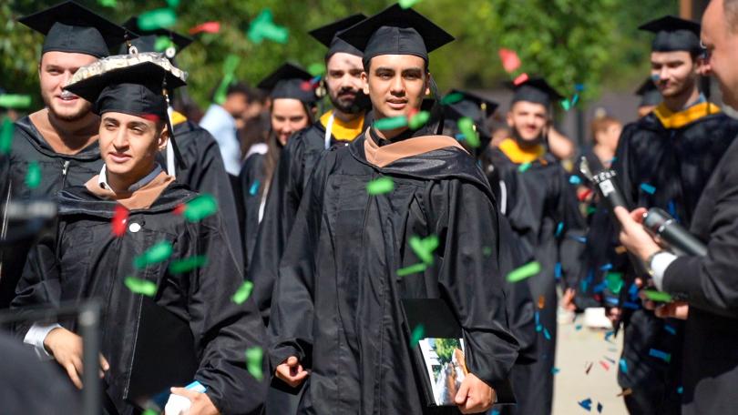 students wearing graduation robes walk through falling confetti 
