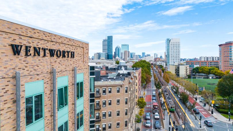 An exterior view of 525 Huntington as shot by a drone showing the Wentworth sign on the building and Boston in the background
