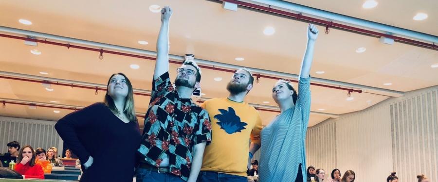 four students standing with their arms raised triumphantly in the air