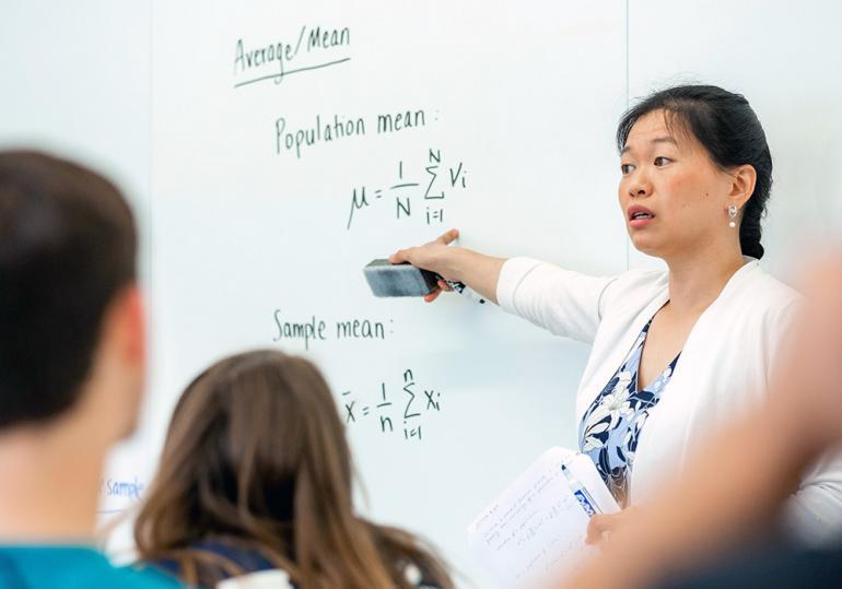 Math professor writing problem on white board.