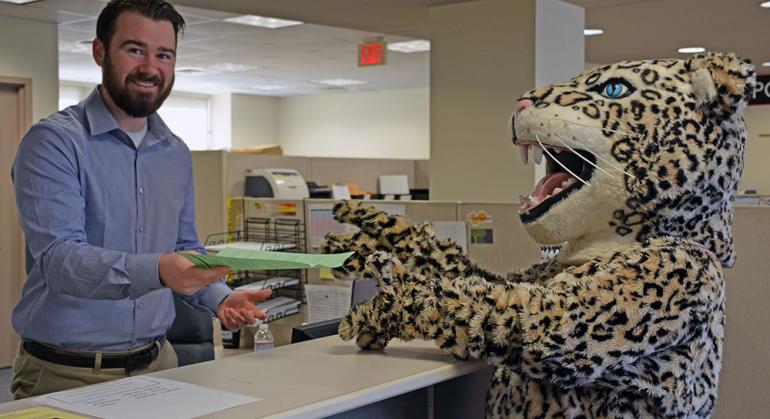 Leopard mascot accepting paper from man behind a counter.