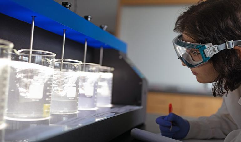 Woman conducting tests in lab, recording results in notebook.