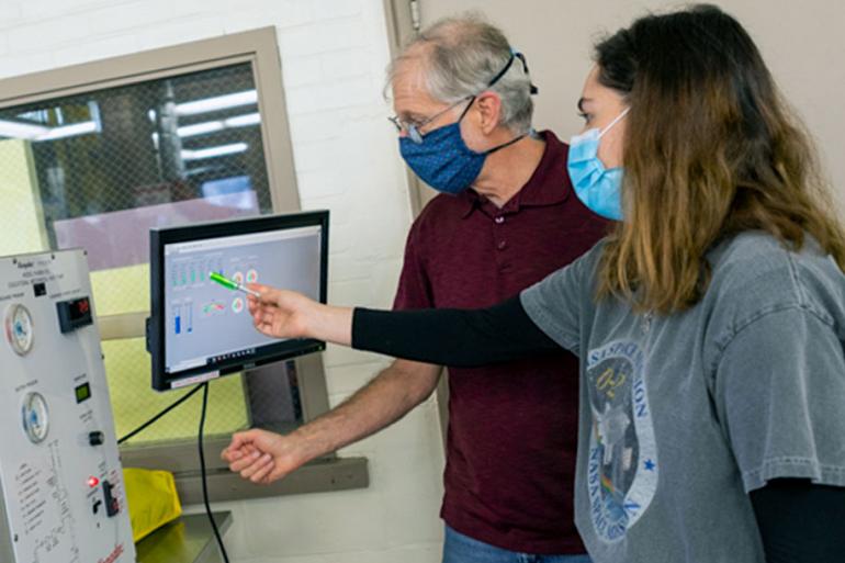 A female student points at a computer screen while a faculty member looks on.