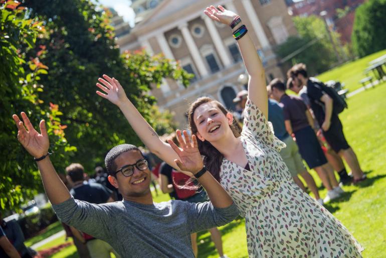 A male and female student look at the camera with their arms raised.