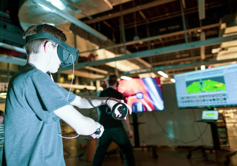 Two male students test out VR headsets in front of televisions