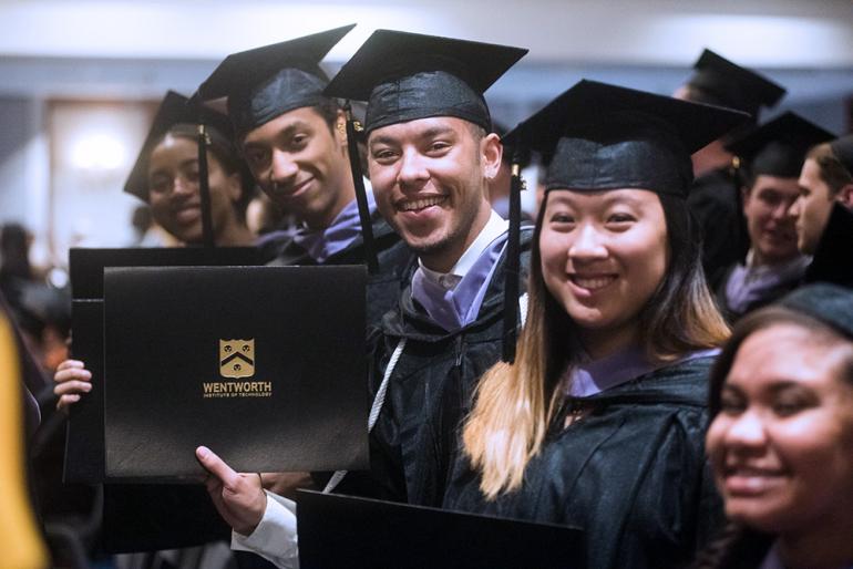 Students in caps and gowns holding up diplomas.