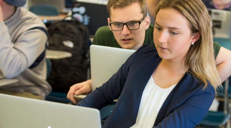 Two students, a male and female, look at a laptop together