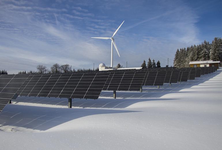 A snowy landscape with a wind turbine in the background and a solar array in the foreground. 