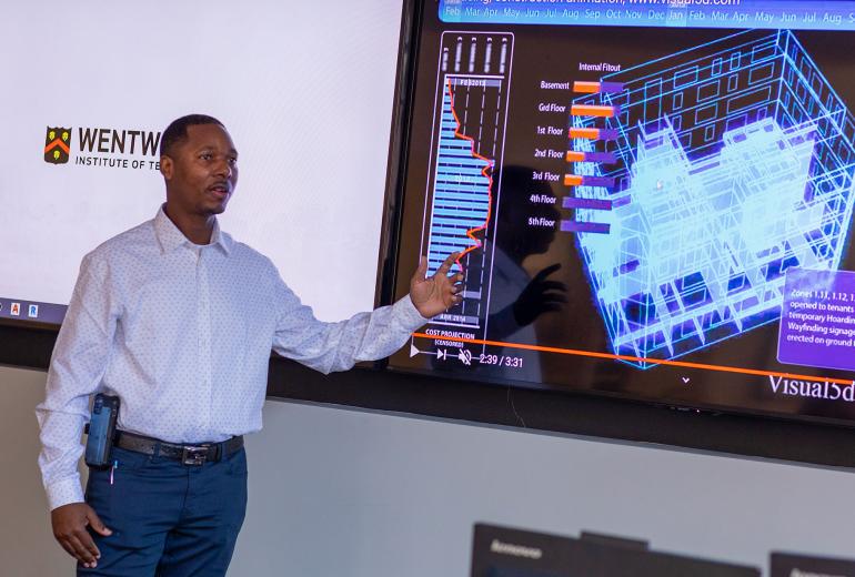 A man points at a projection in front of a classroom. 