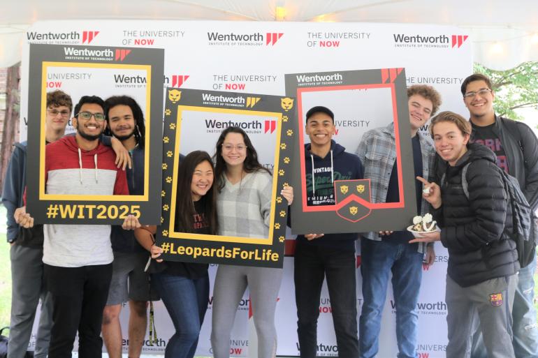 Students posting with photo frames in front of Wentworth banner