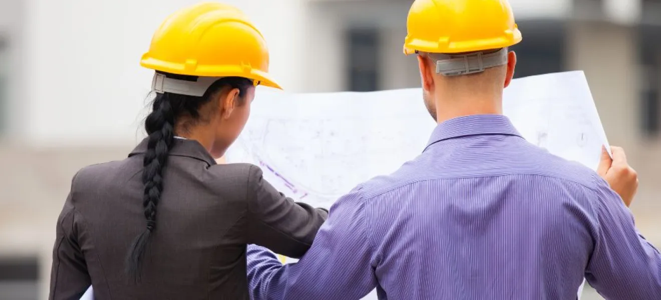 two people in hard hats look at blueprints