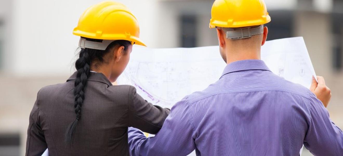 two people in hard hats look at blueprints