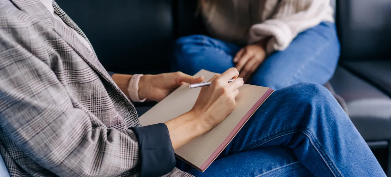 two people having a conversation on a couch, one has a notepad, you can't see either of their heads