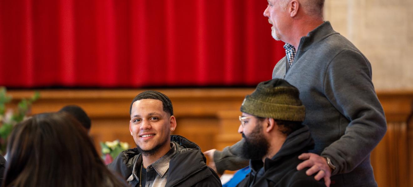 standing man greeting two other men sitting down